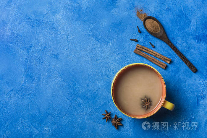 暖饮马沙拉茶黄杯子里有香菜木勺里有肉桂和玫瑰梗背景是经典的蓝色