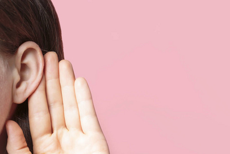 粉色话女孩用手掌放在耳朵上仔细听,在粉色背景上的特写,新闻概念照片