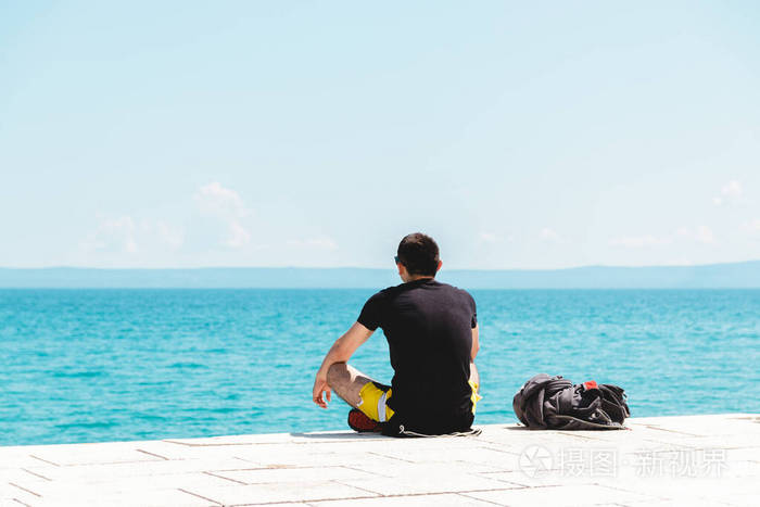 年轻的旅行者独自一人背着背包沉思着望着大海享受着寂静