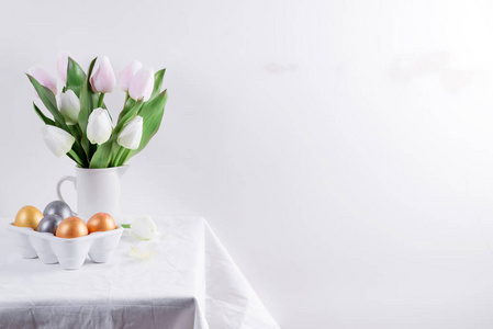 金色复活节彩蛋，白色桌子上有郁金香。复活节背景或复活节概念。