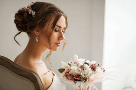 在明亮的白色工作室里，年轻的新娘穿着漂亮的裙子拿着一束花。婚礼概念。