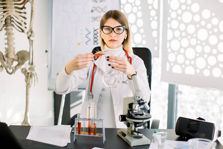 漂亮的白种女研究员博士化学家实验室里拿着玻璃设备。女专业科学家将红色溶液从试管中净化成玻璃瓶。实验室临床分析概念