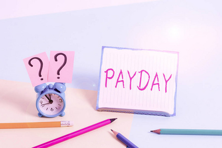 文字写作发薪日。一天的商业概念，某人被支付或期望被支付他们的工资微型闹钟旁边的文具倾斜放置在柔和的背景。