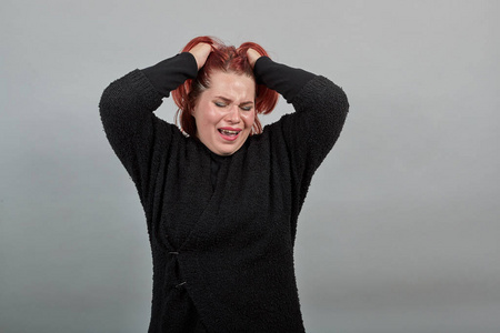 穿着黑色毛衣的年轻胖女人心烦意乱地哭着,手挽着头发照片