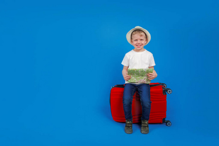 持旅游卡的儿童游客坐在红色旅行箱上，在地图上看到蓝色背景。一个旅游的概念，一个文本的地方。