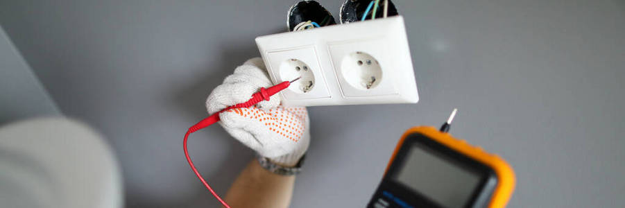 戴手套的修理工用螺丝刀测试电流和固定插座