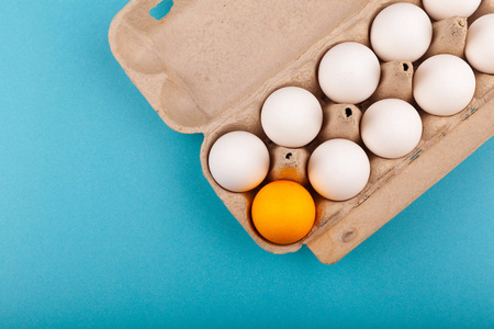 鸡蛋鸡蛋。打开的灰色盒子的俯视图，蓝色背景上有白色的鸡蛋。一个颜色不同的鸡蛋，一个橙色的鸡蛋。专注的概念，一个被抛弃的人，不像其