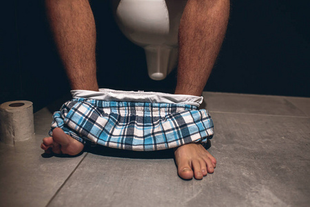 男人坐在厕所或厕所的锅上.排便.一个人在休息室.纸卷在左边.照片