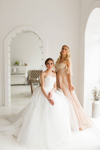 在明亮的白色工作室里，两个穿着漂亮裙子的年轻新娘。婚礼概念。