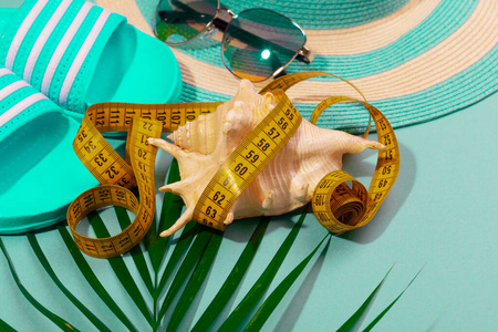 条纹帽子太阳镜带贝壳和棕榈枝的卷尺在绿松石蓝色背景上的俯视图。在海上度假减肥的概念。广告空间