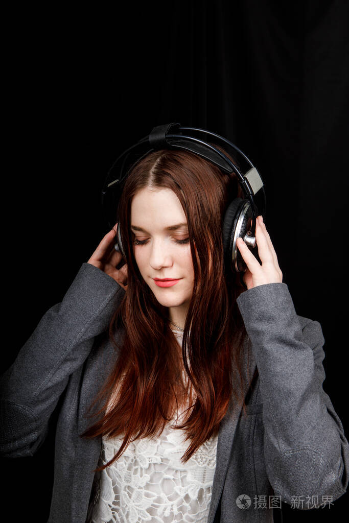 年轻漂亮的女人戴着耳机听音乐.黑底灰色夹克的女孩.