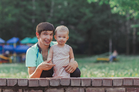 父亲和他的小女儿站在公园背景的喷泉旁