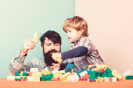 父子玩游戏。爸爸和孩子用塑料块做的。父子俩用砖头创造了五彩缤纷的建筑。儿童保育发展和养育。长胡子的父亲和男孩一起玩