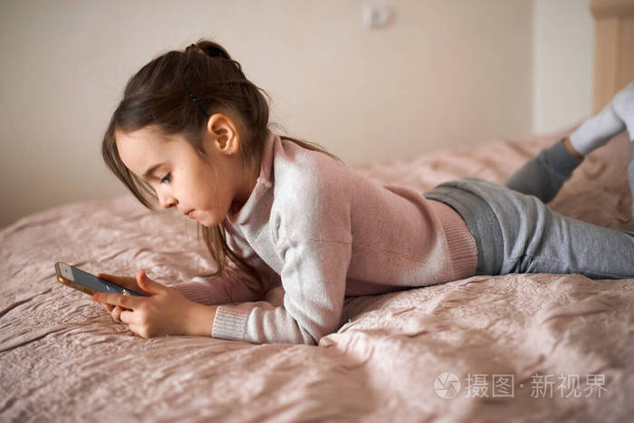可爱认真的女孩躺在床上拿着手机床关闭俯视照片