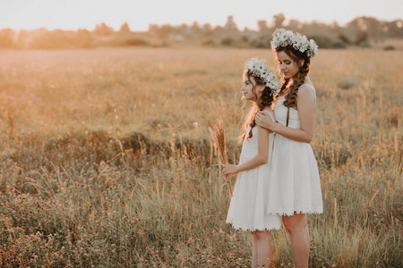 夕阳下，母亲和女儿一起穿着白色连衣裙，扎着辫子，戴着波西米亚风格的花环