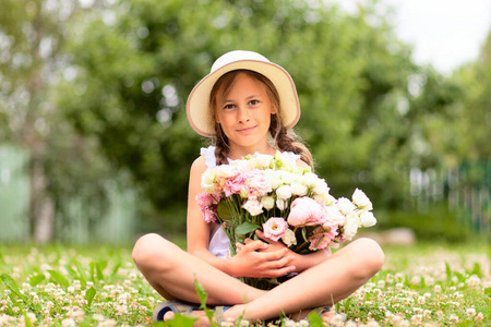 拿着一大束牡丹花的女孩。一个戴着宽边帽的少年坐在一片花草盛开的草地上。