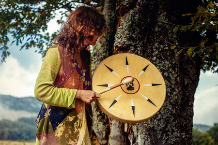 美丽的萨满教女孩在大自然中的萨满框架鼓.照片