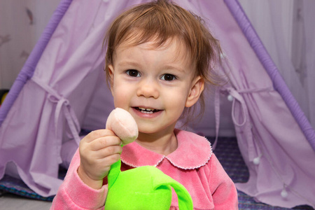 2岁的小女孩微笑着在儿童房里展示五颜六色的玩具。