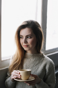 A girl drinking coffee in the kitchen at home. Young woman holdi