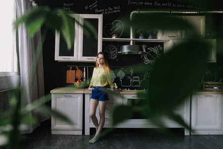 A girl drinking coffee in the kitchen at home. Young woman holdi