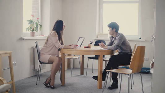 年轻的亚洲男人在桌子旁和自信的女商人交谈。多民族的人在时髦的现代办公室里聊天。