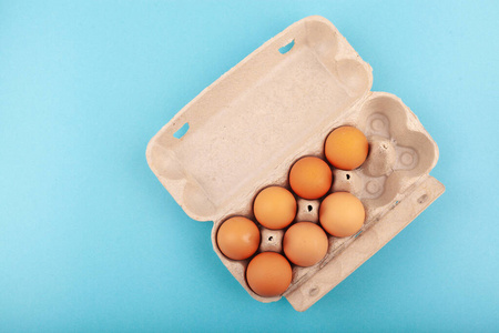 鸡蛋鸡蛋。一个打开的灰色盒子的俯视图，棕色的鸡蛋被隔离在蓝色的背景上。健康生活方式的概念，获取纯蛋白质。适当的早餐。七个鸡蛋。