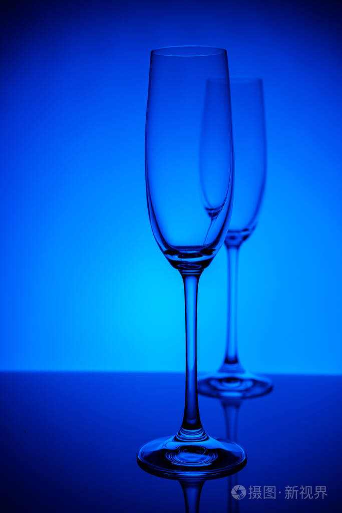 两个空香槟酒杯反射,深蓝色和黑色背景渐变背景.