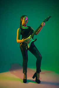 在霓虹灯下绿色工作室背景上孤立的高加索女吉他手肖像