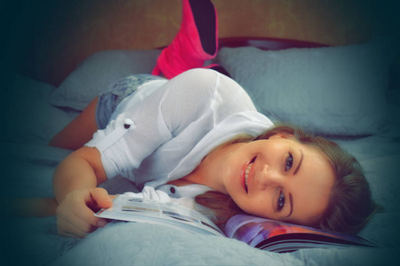 快乐的女人躺在床上。在家看书消遣。女人微笑着享受着幸福