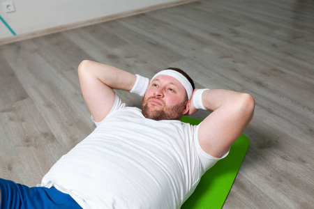 胖子躺在健身馆地板上的绿色垫子上，用最后的力气锻炼腹部肌肉。超重
