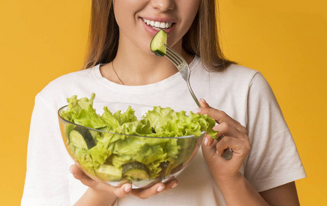 一个面带微笑的女人正在吃黄色背景的新鲜蔬菜沙拉