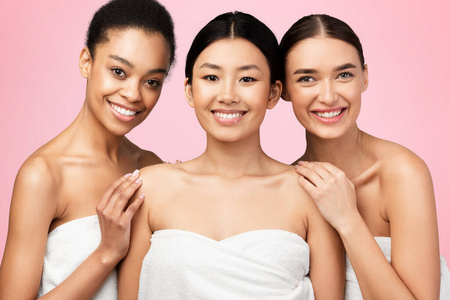 三个漂亮的女孩在粉红色的背景上穿着浴巾摆姿势