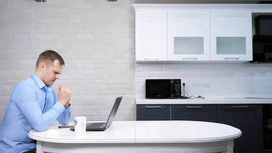 一个商人坐在厨房的桌子旁用他的笔记本电脑