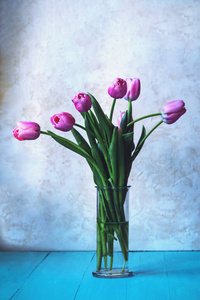 一束粉红色的郁金香在蓝色桌子上的玻璃花瓶里。