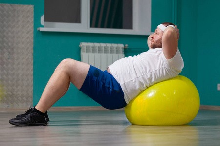 在集体健身课上,超重男子躺在健身球上.