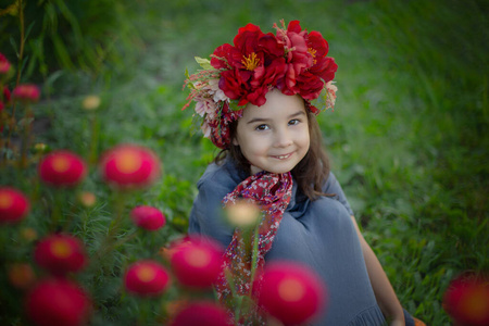 一个戴着红色花冠的小女孩坐在开着勃艮第康乃馨的花丛下照片