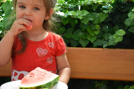 有趣的画像一个难以置信的美丽小女孩吃西瓜，健康的水果零食，可爱的卷发幼儿。