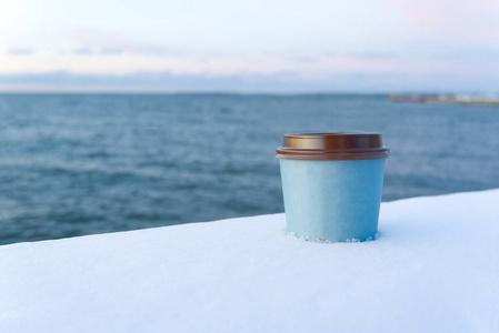 冬天带着海味的咖啡外卖。冬天的雪带走咖啡杯日落在海上