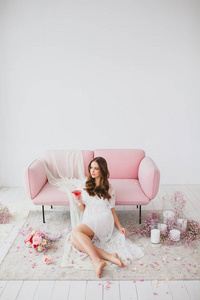 工作室里，穿着白色睡衣的年轻新娘在玫瑰沙发旁摆姿势
