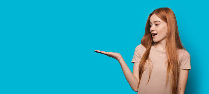 高加索人女士在一堵空白的蓝色墙上摆姿势,手掌上拿着什么东西照片