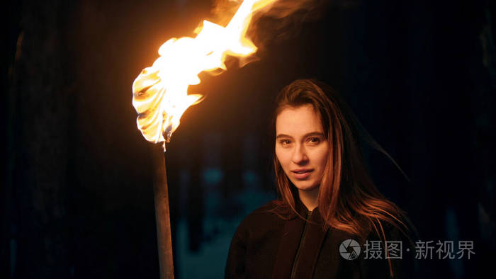 年轻美丽的微笑女人拿着火炬在夜色森林里看着镜头