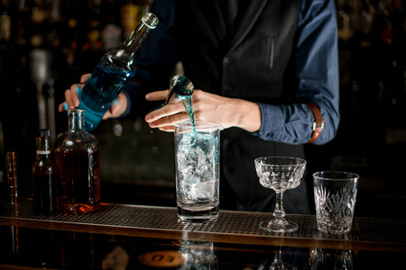 调酒师从装有蓝色酒精饮料的瓶子里量出鸡尾酒的成分。