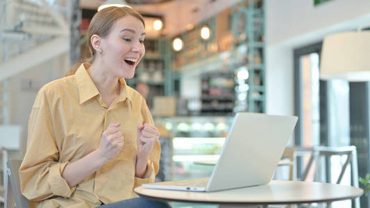 年轻女子在咖啡厅用笔记本电脑庆祝成功