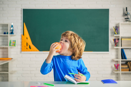 友好的孩子在黑板桌旁边的教室里吃苹果。小学教室。儿童科学教育观。