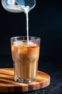 在黑暗背景下，用高玻璃杯把牛奶倒进冰咖啡里。Concept清爽夏日饮品
