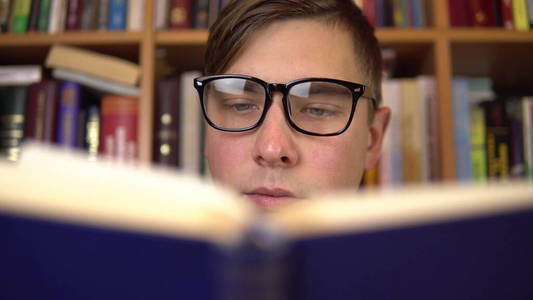 一个戴眼镜的人仔细地看了看这本书的特写.背景是书架上的书.