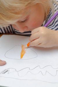 一个金发小女孩用铅笔在纸上画画。