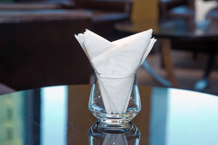 模糊图像白色餐巾纸放在宴会厅桌子上的玻璃上。酒店餐厅提供装饰餐巾玻璃餐具的酒店餐桌。