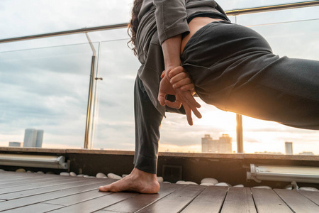 日落背景下，一名男子在摩天大楼屋顶上练习瑜伽。三色帕司