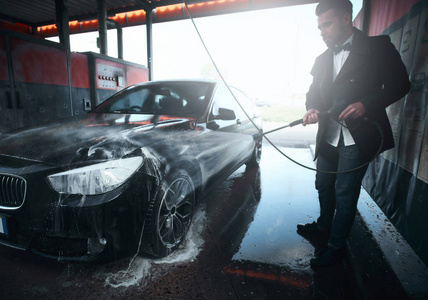 一名男子在室外的洗车站用喷水器清洗他的黑色汽车